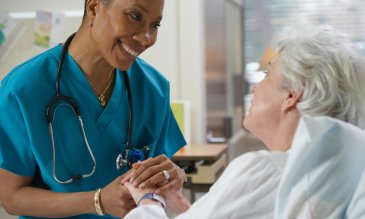 Female medical professional holds hand of elderly patient while talking and smiling