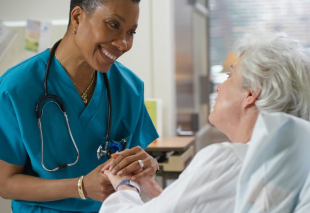 Female medical professional holds hand of elderly patient while talking and smiling