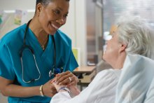 Female medical professional holds hand of elderly patient while talking and smiling