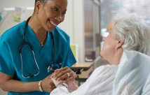 Female medical professional holds hand of elderly patient while talking and smiling